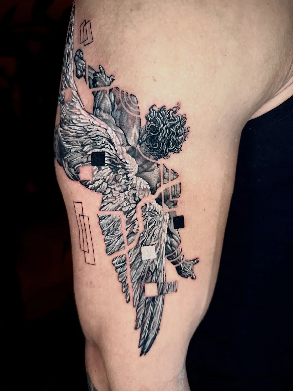 Winged angel statue with glitch effect, black and grey upper-arm tattoo