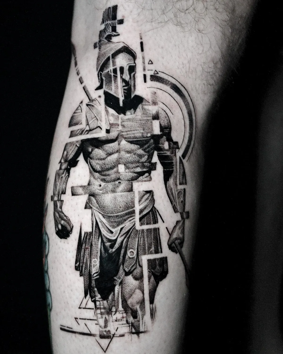 Glitch-style spartan warrior with geometric fragments, black and grey leg tattoo