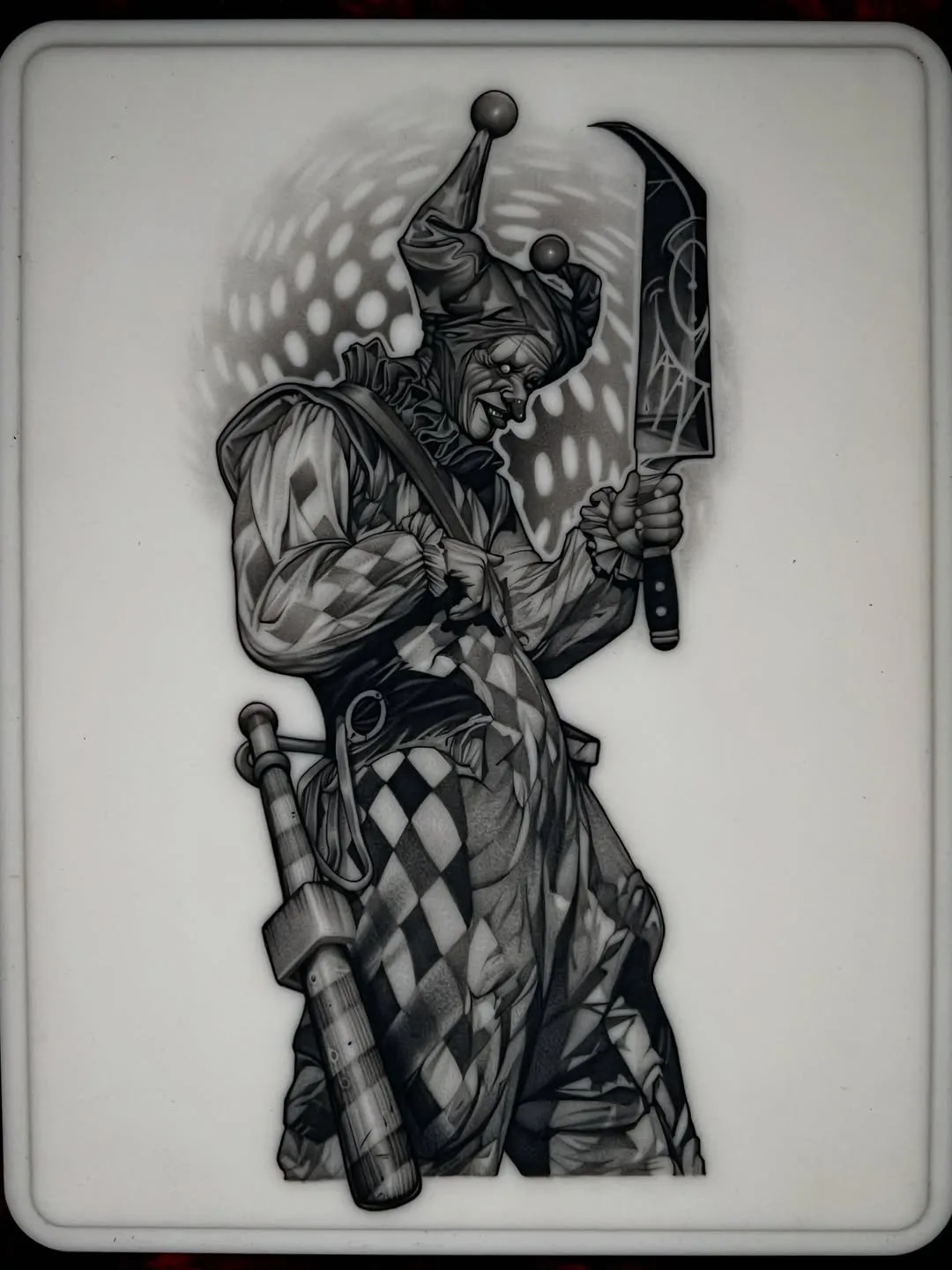 Menacing harlequin jester raising a cleaver, black and grey piece tattooed on fake skin